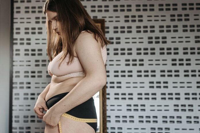 choisir-sous-vetements-morphologie-femme-guide Confident young woman measures her hips in a stylish interior, embracing body positivity.