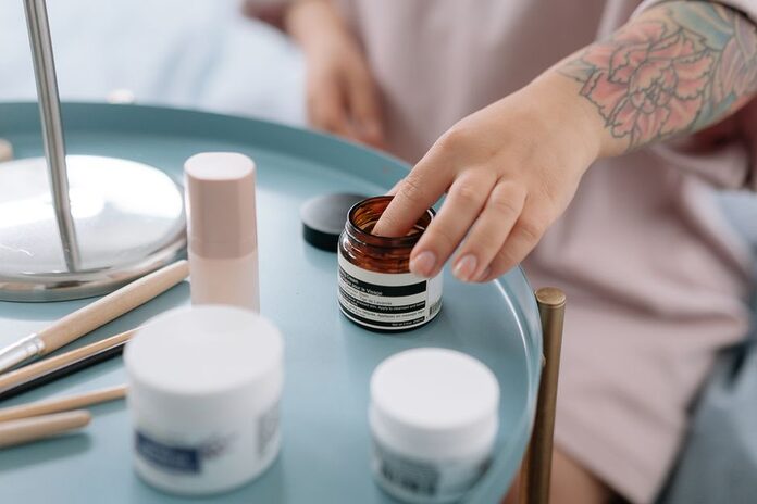 morphologie-femme-ronde-skincare-routine-carnation-besoins A close-up shot of a hand reaching for skincare creams on a blue tray indoors.