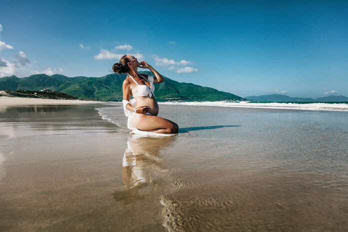 skincare-routine-femme-enceinte-ete-2026 Pregnant woman posing on a wet sandy beach